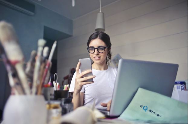 Woman looking at smartphone sitting in front of laptop - podcasts article