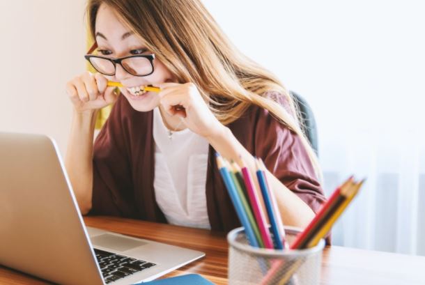 Unusual ways to relieve work stress - woman at laptop biting pencil