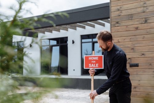 Man placing a ‘home for sale’ sign outside a house