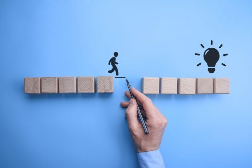 A businessman draws a bridge between two sets of blocks, indicating triumph over obstacles.