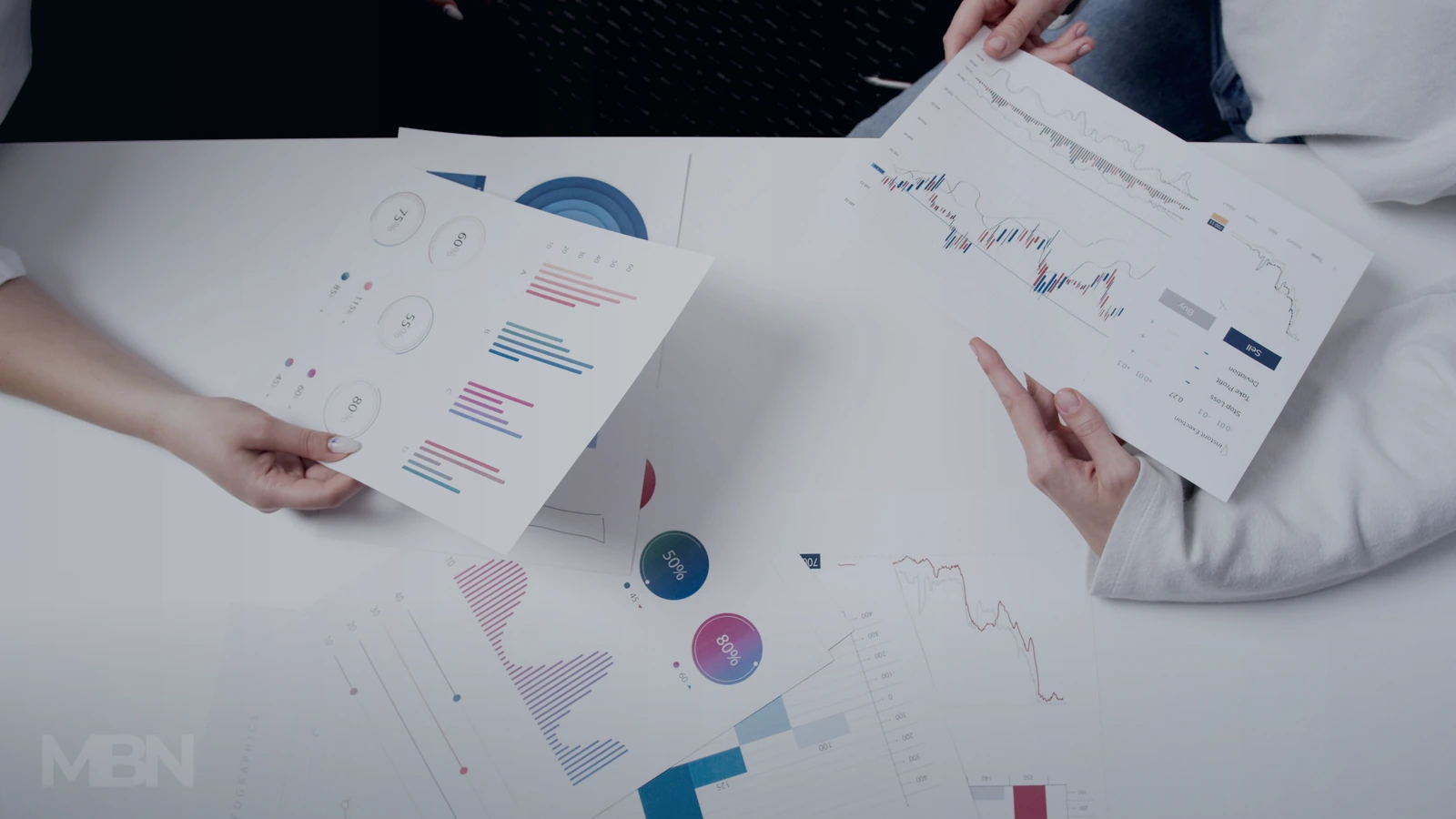 Blue-toned editorial cover showing several hands comparing printed business charts across a shared meeting table.