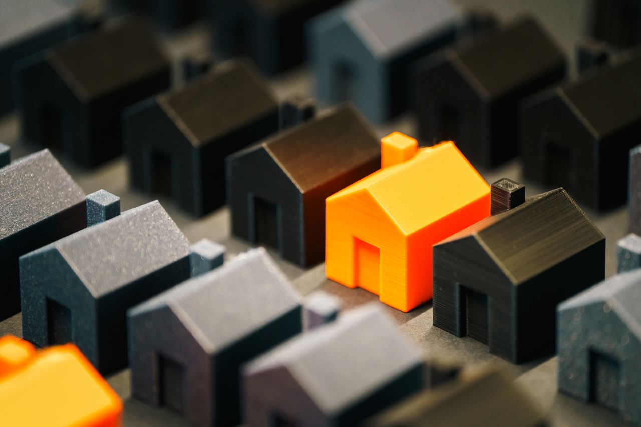 Striking orange model house stands out among black miniature houses, symbolizing real estate choices