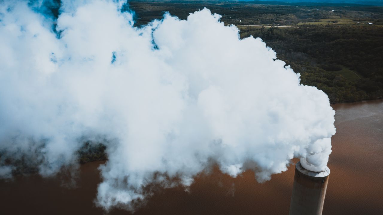 Aerial shot capturing dense smoke from an industrial smokestack by the river