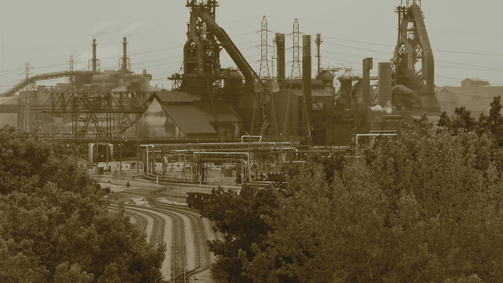 Editorial cover showing a steel mill and rail tracks, representative of heavy industry. Image by Roy Luck, CC BY 2.0 via Wikimedia Commons.