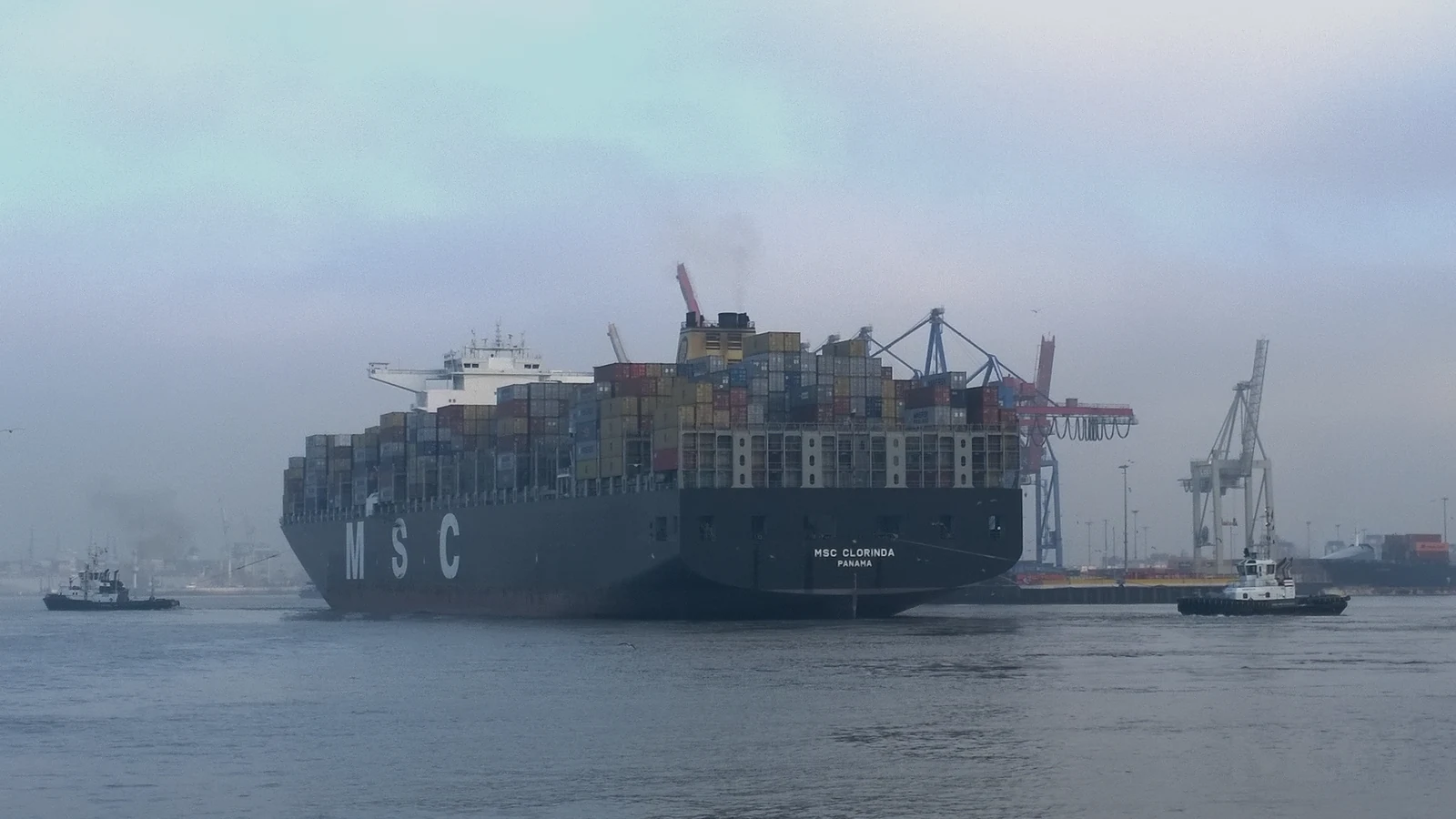 Editorial cover showing a container ship beside port cranes, representative of global trade. Image by Hummelhummel, CC BY-SA 3.0 via Wikimedia Commons.