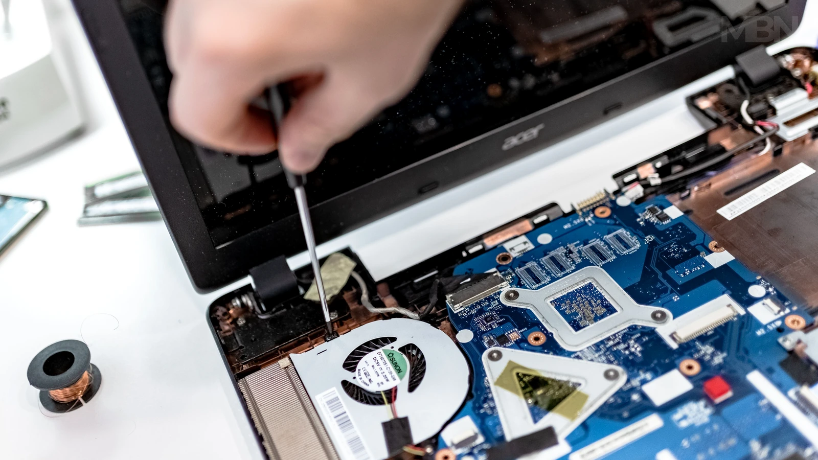 A hand uses a screwdriver inside an opened Acer laptop, with a blue motherboard, cooling fan, and other components visible.