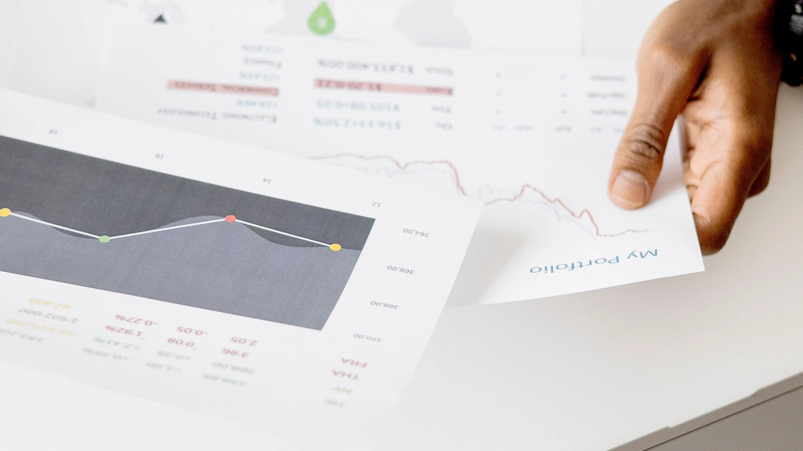 A hand reviews printed charts beside a laptop in a representative business-analysis photograph by Hanna Pad/Pexels.