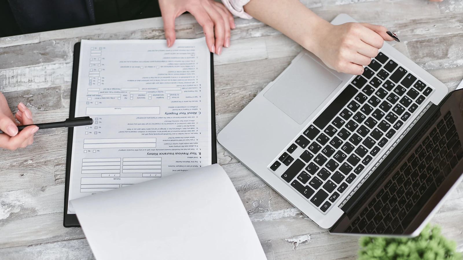 Two people review paperwork beside a laptop on an office table, a representative stock photograph by Mikhail Nilov/Pexels.