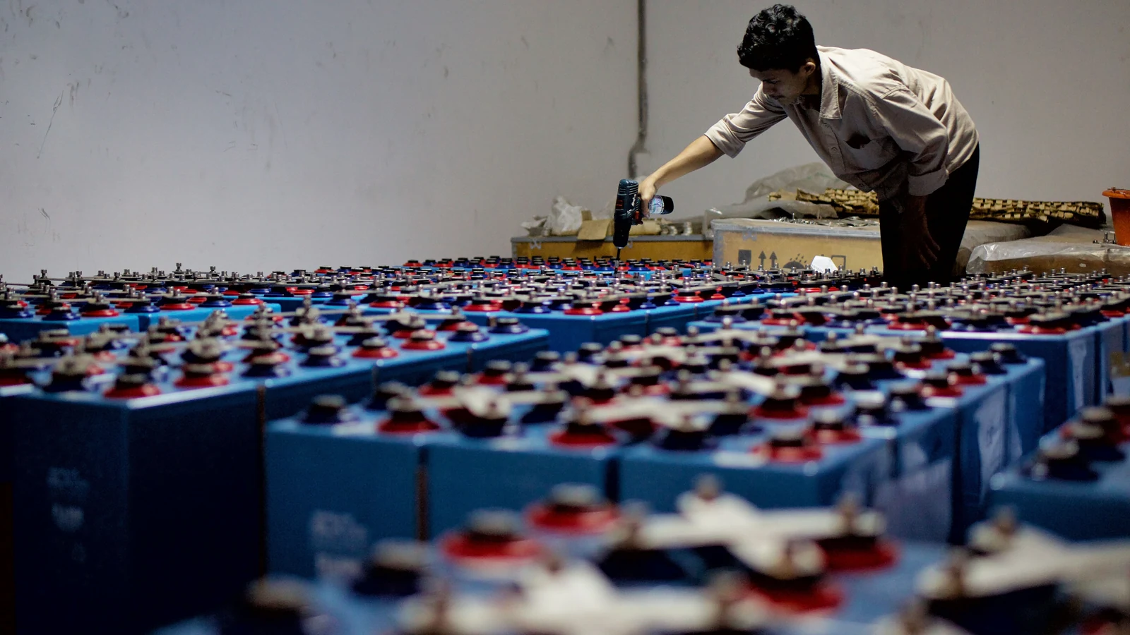 A worker checks rows of industrial batteries indoors. Representative photograph by Heru Dharma via Pexels.