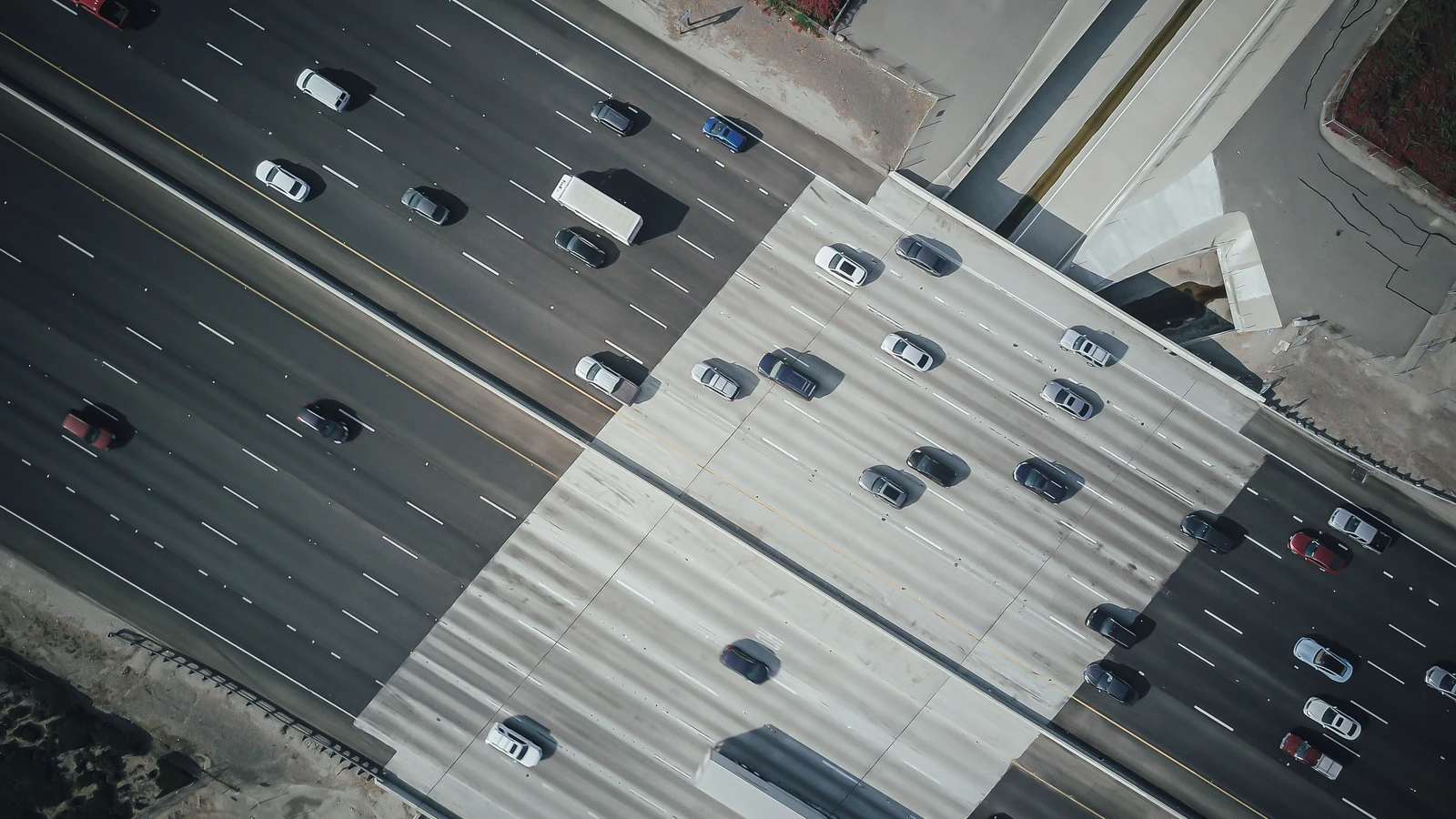 Cars and trucks travel along a multilane highway beneath an overpass, a representative stock photograph by Kindel Media/Pexels.