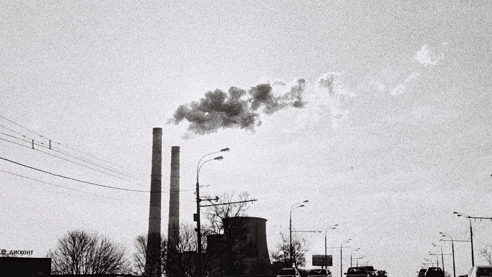 Vehicles pass industrial stacks beneath a cloudy sky in a representative black-and-white photograph by Глеб Серебренников/Pexels.