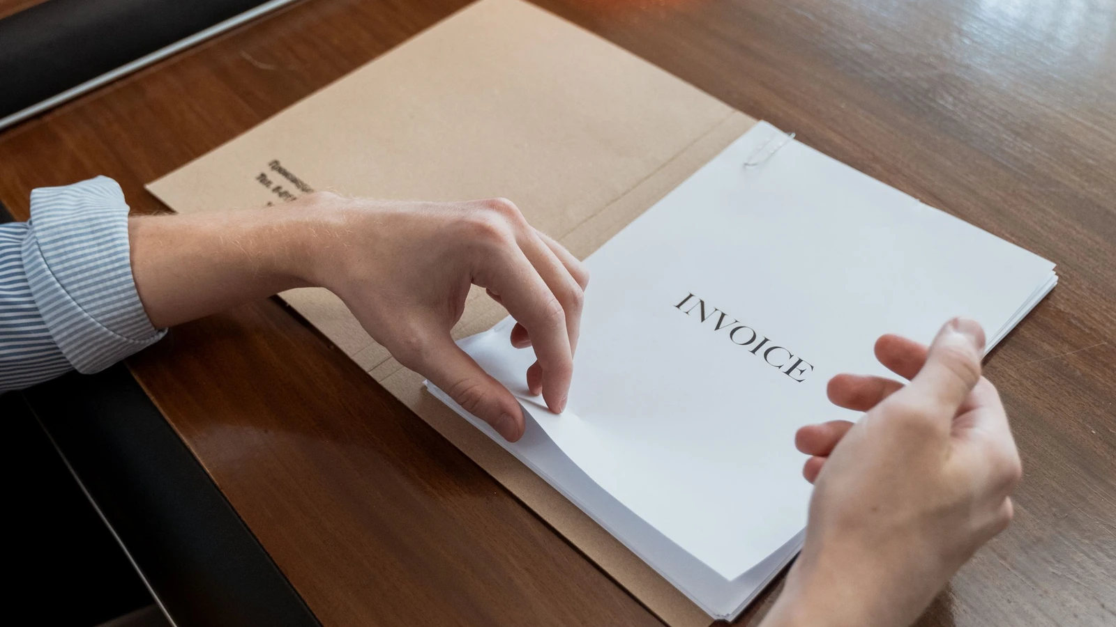 Hands holding invoice paperwork over a wooden desk, a representative business administration photograph by MART PRODUCTION/Pexels.