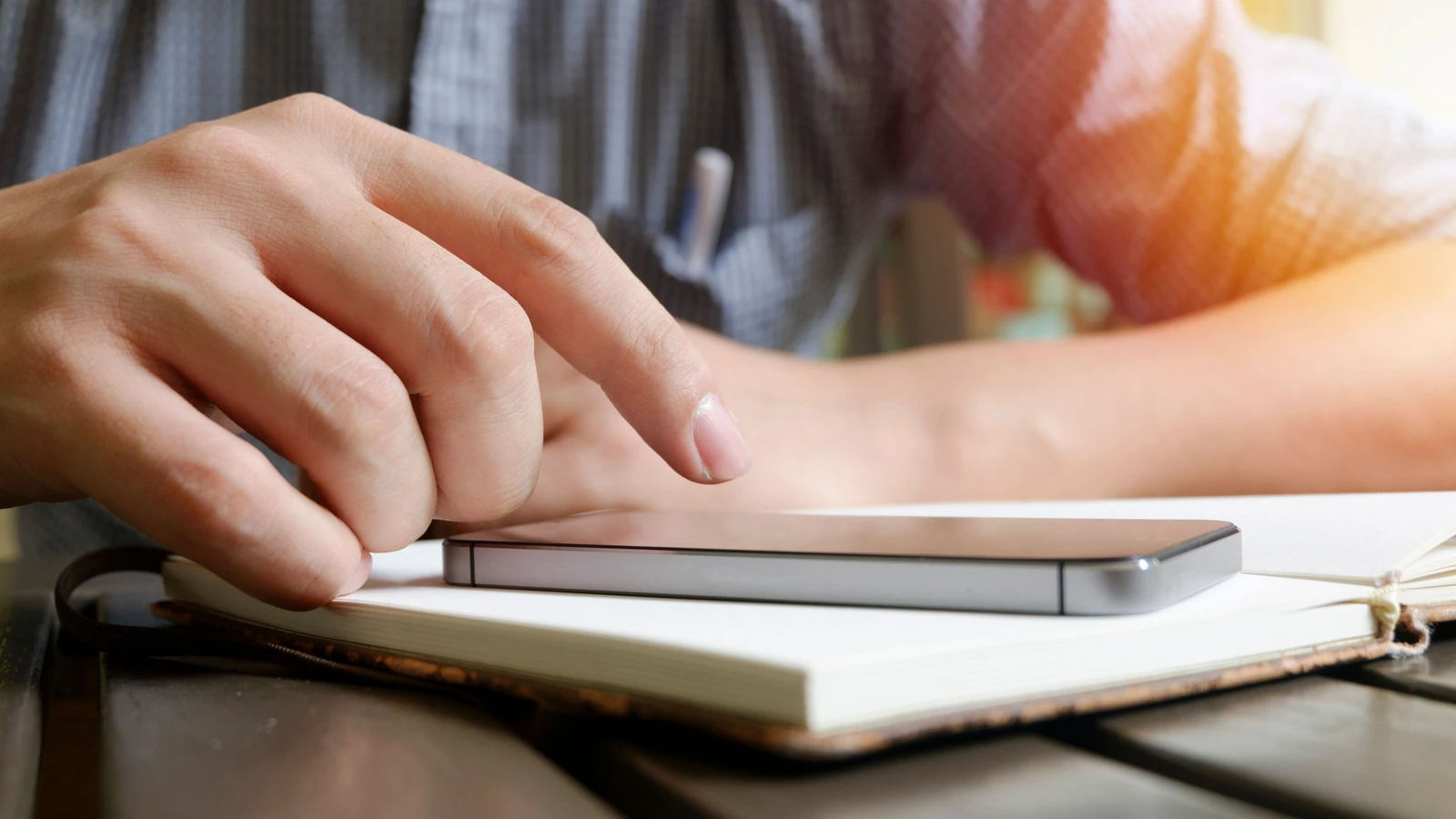 A hand using a smartphone beside a notebook, representative stock photography by Porapak Apichodilok/Pexels.