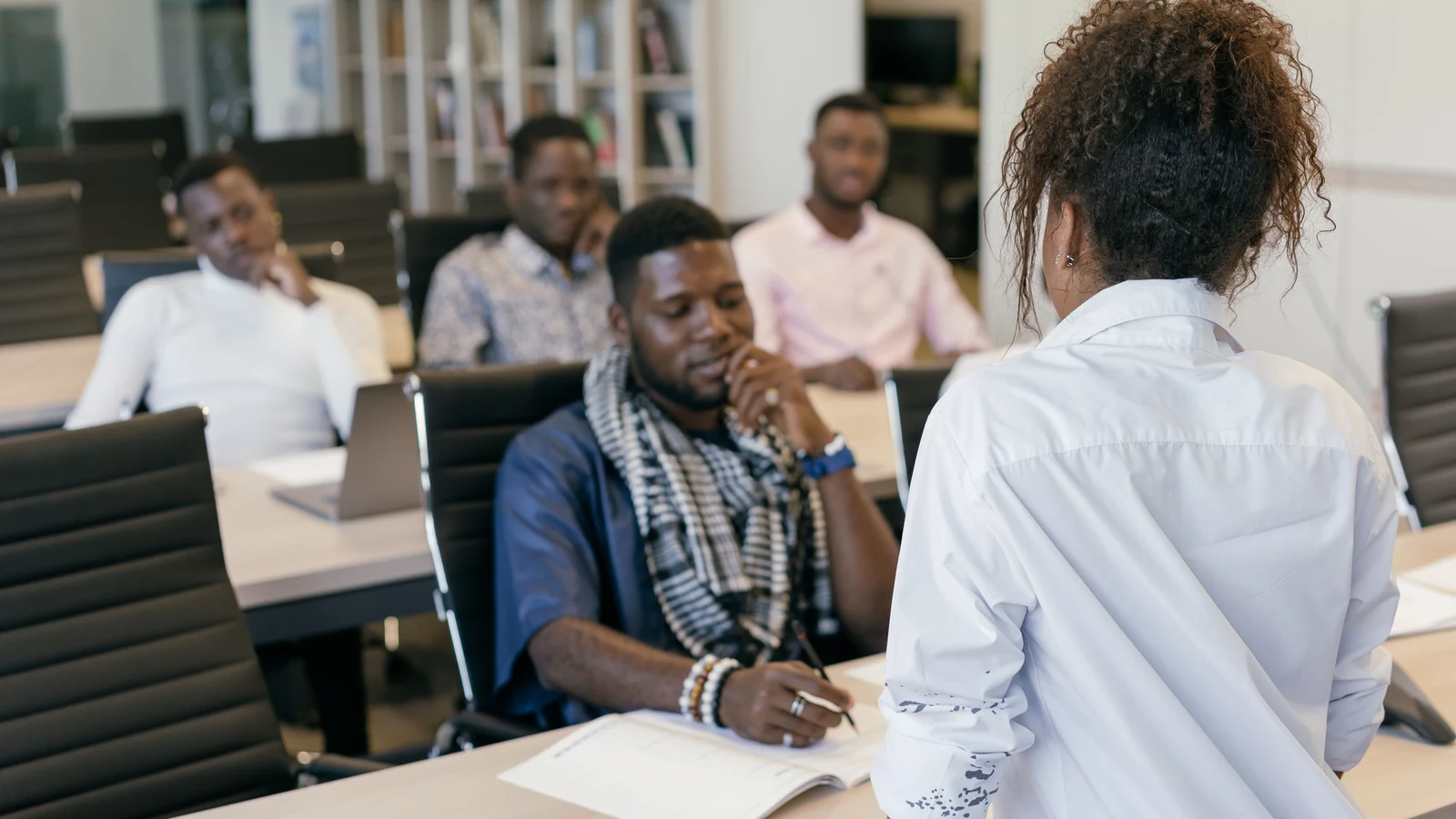 A presenter addresses adults seated at desks during a training session, a representative stock photograph by Mikhail Nilov/Pexels.