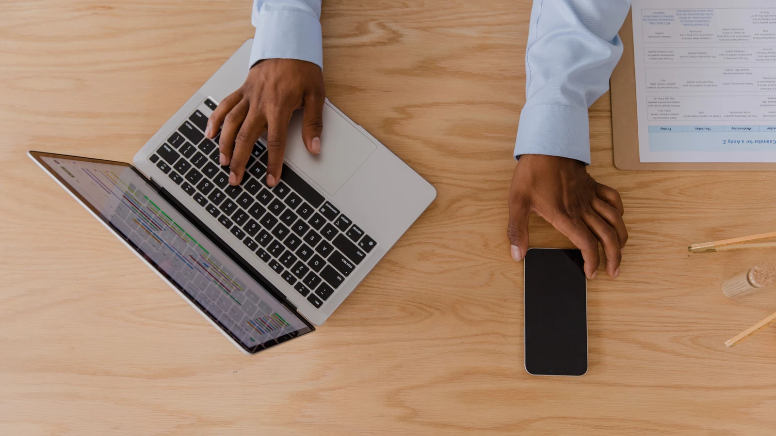 Hands beside a smartphone and an open laptop on a wooden desk, a representative stock photograph by RDNE Stock project/Pexels.