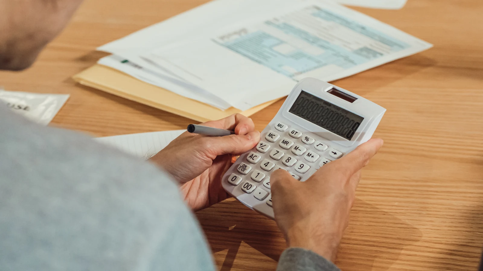 Hands using a calculator beside financial documents on a desk, a representative stock photograph by Kindel Media via Pexels.