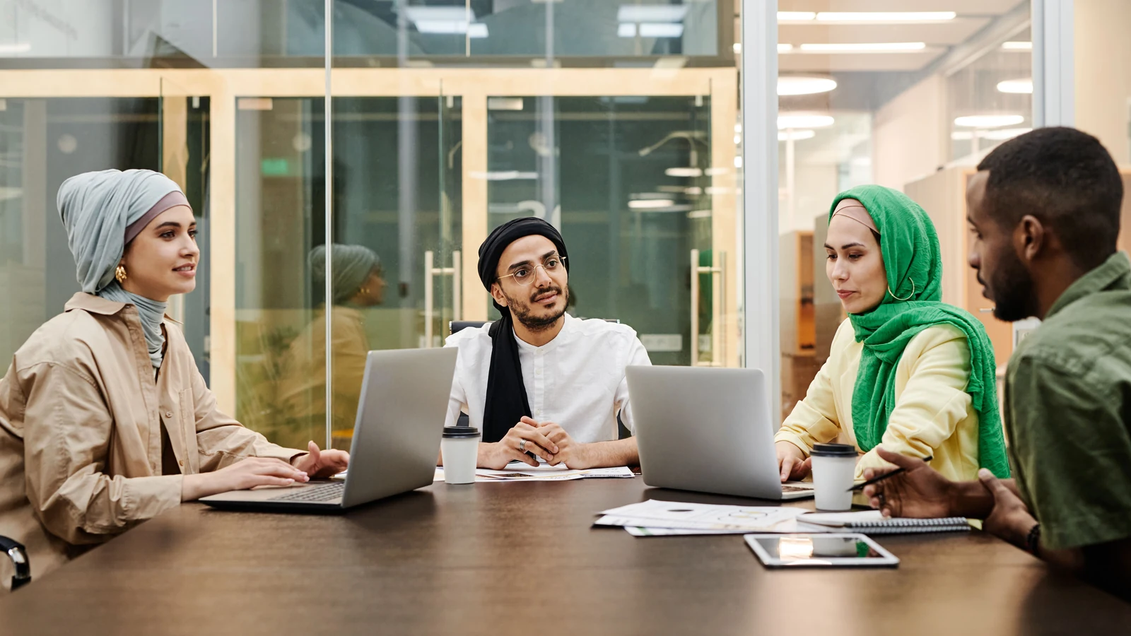 Colleagues discuss work around a table with laptops in an office; representative stock photograph by Edmond Dantès/Pexels.
