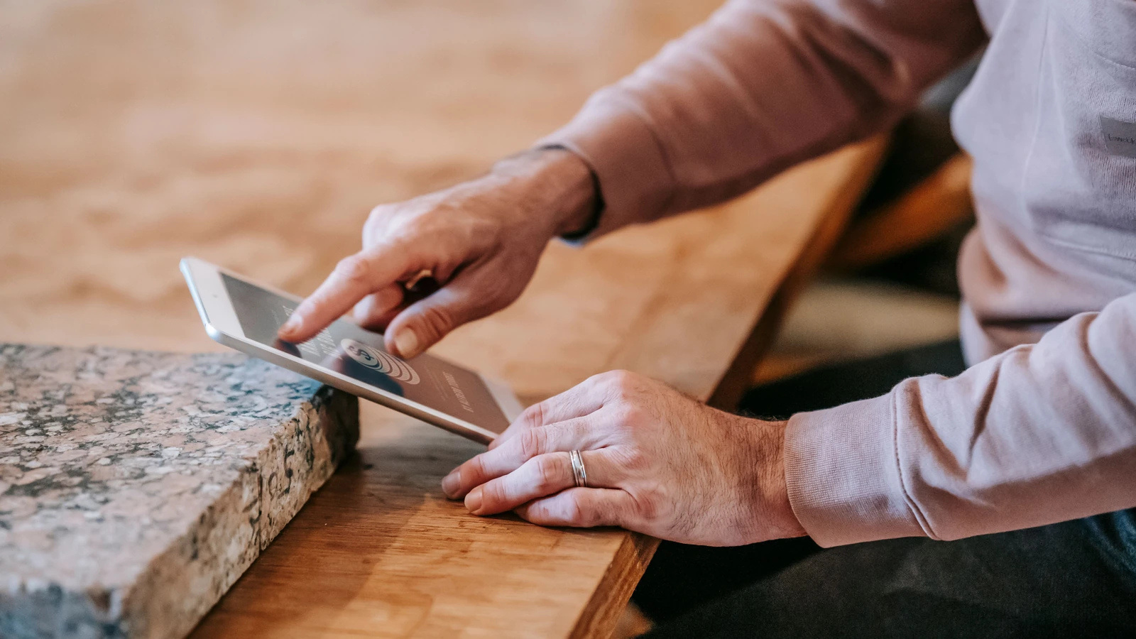 Hands holding a tablet over a wooden table, a representative digital service photograph by Gary Barnes/Pexels.