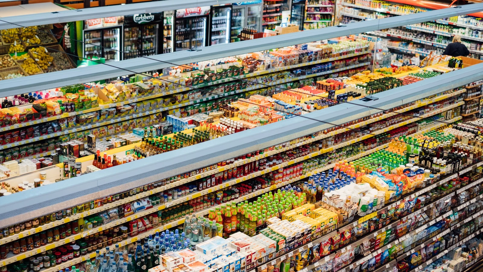 An overhead view of stocked supermarket shelves appears in a representative photograph by freestocks.org/Pexels.