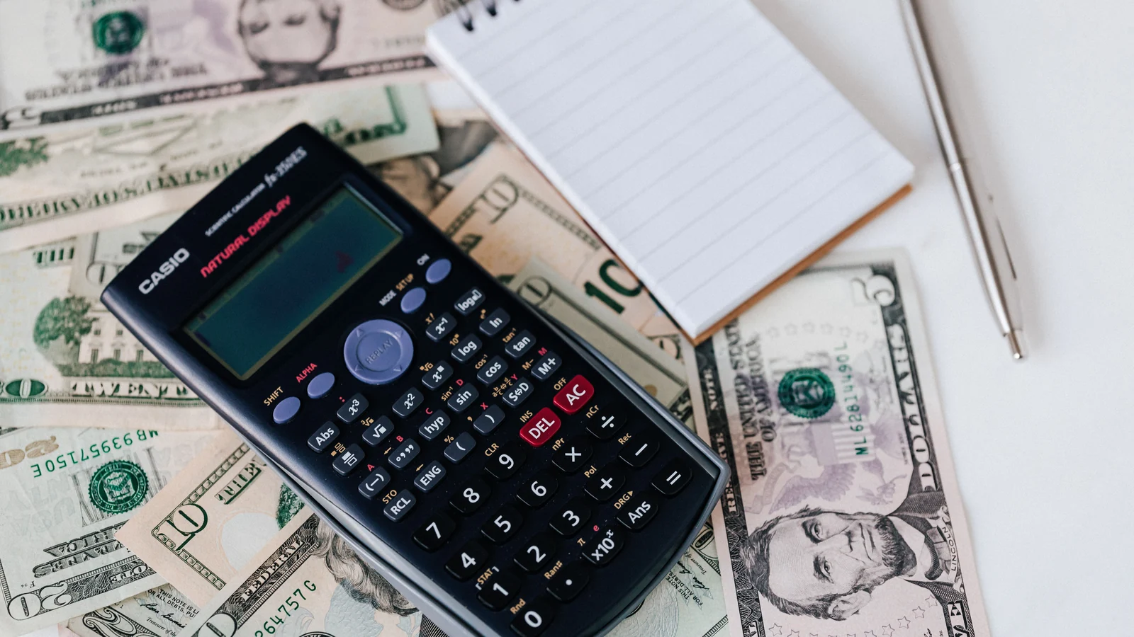 A calculator, notebook and pen rest on US dollar bills, a representative household-finance stock photograph by Kaboompics on Pexels.