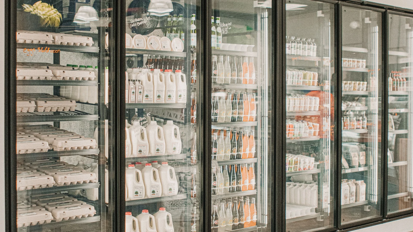 Glass-fronted grocery refrigerators display dairy products and drinks in a representative stock photograph by Daniel & Hannah Snipes/Pexels.