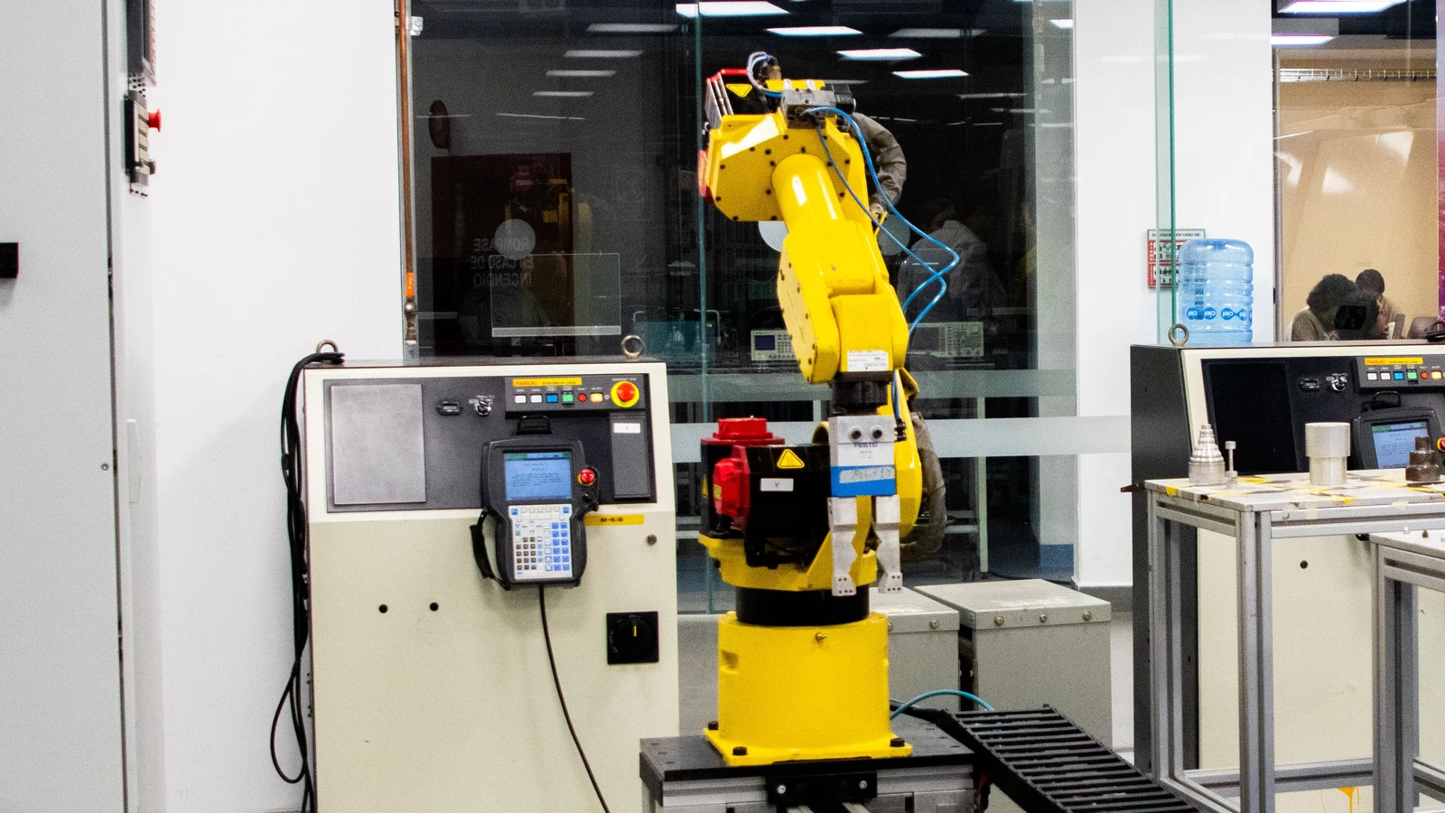 Yellow industrial robot arm, control cabinet and conveyor equipment, shown in a representative stock photograph by Ludovic Delot under the Pexels License.