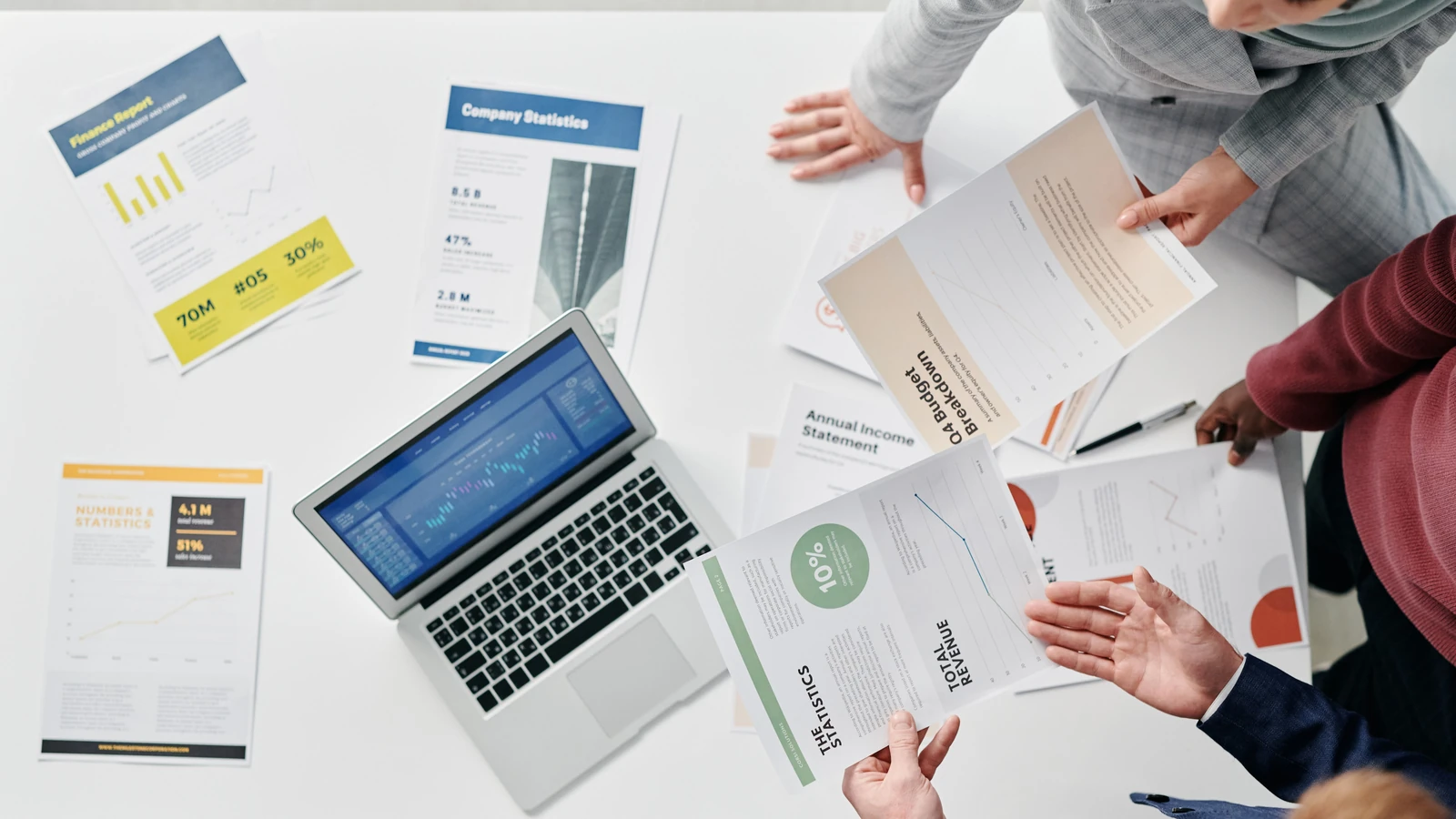 Colleagues review printed charts around a laptop during an office meeting, a representative stock photograph by Tiger Lily/Pexels.