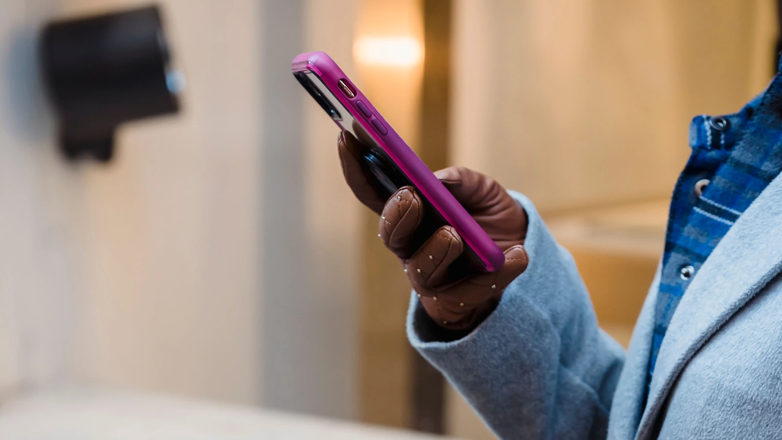 Close-up of a person in a blue coat holding a smartphone, representing customer contact; photograph by Tim Douglas/Pexels.