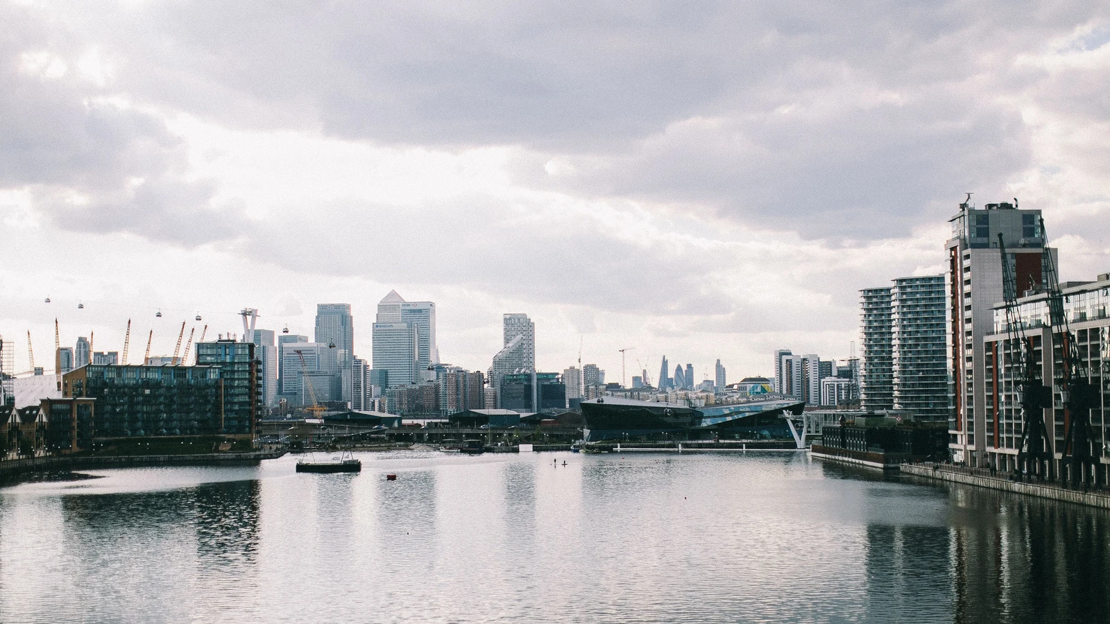 London’s Canary Wharf skyline rises beyond a waterfront under cloudy skies; stock photograph by Lina Kivaka/Pexels.