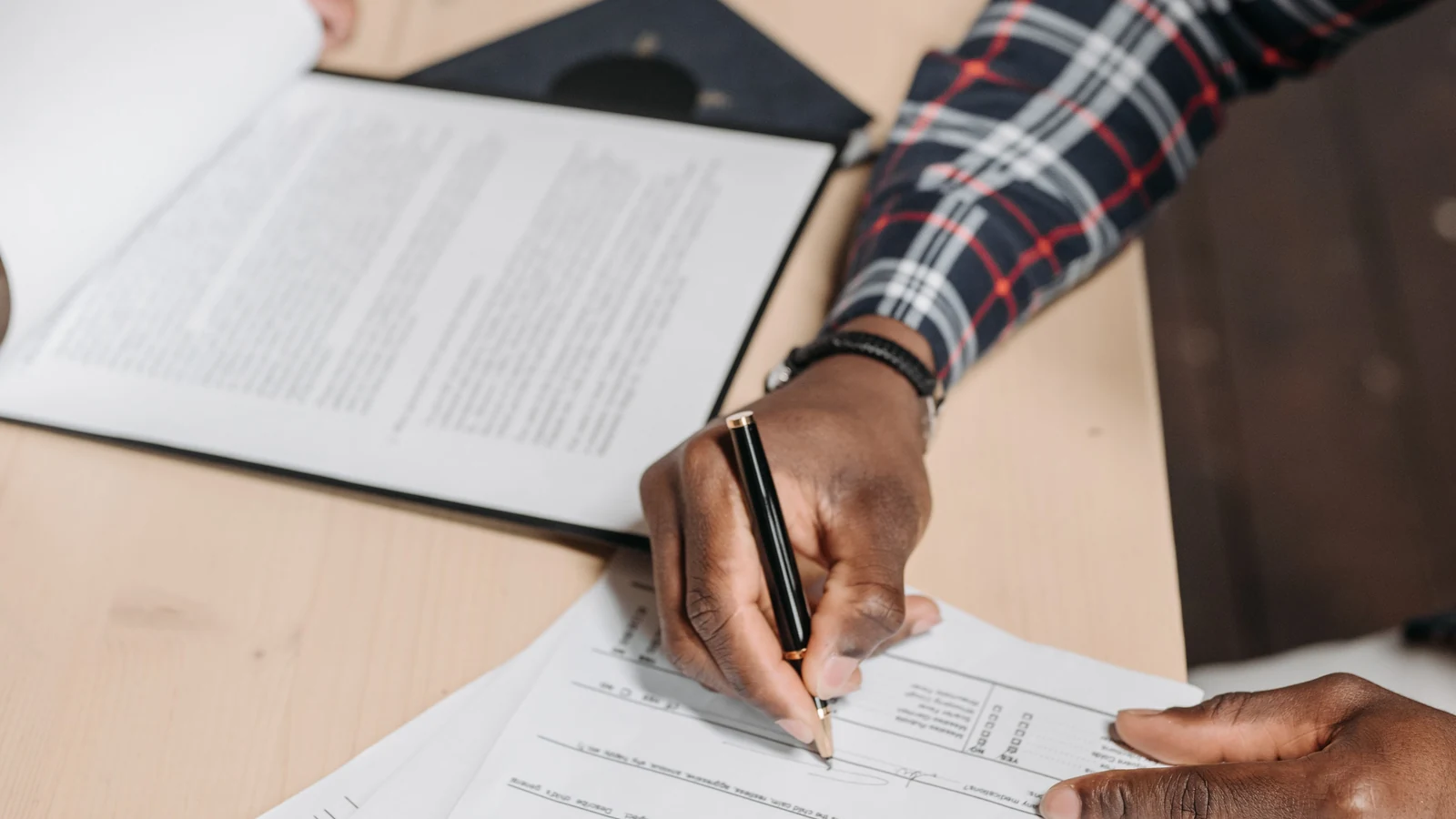 Hands holding a pen over printed documents on a desk, a representative stock photograph by Pavel Danilyuk via Pexels.