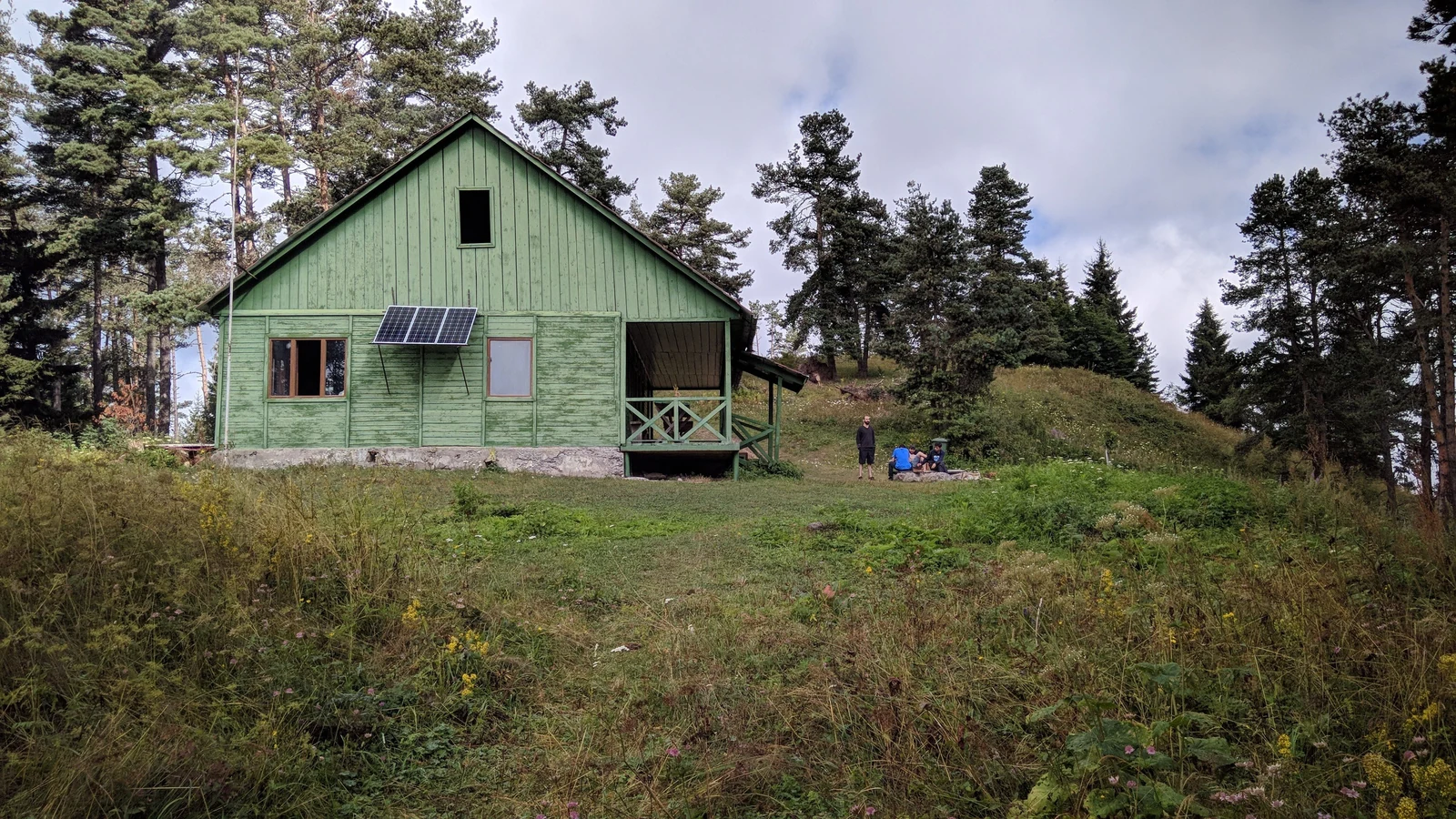 A solar panel mounted on a green wooden house in a rural landscape. Representative photograph by Nika Khutsishvili via Pexels.