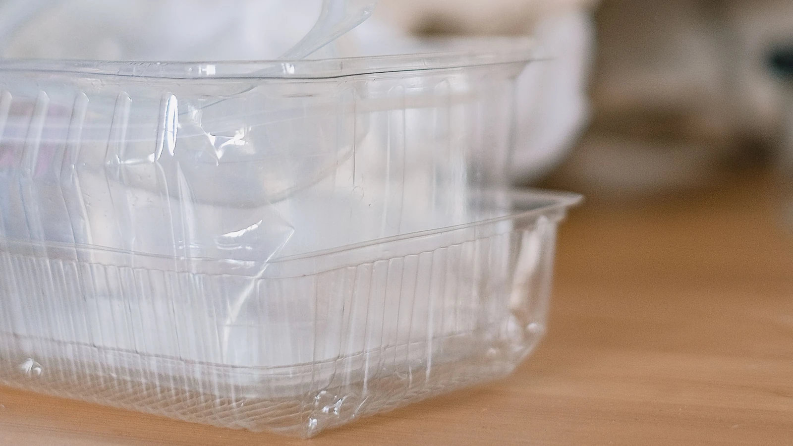 Clear plastic food containers stacked on a wooden table, with paper in the background; photo by SHVETS production via Pexels.