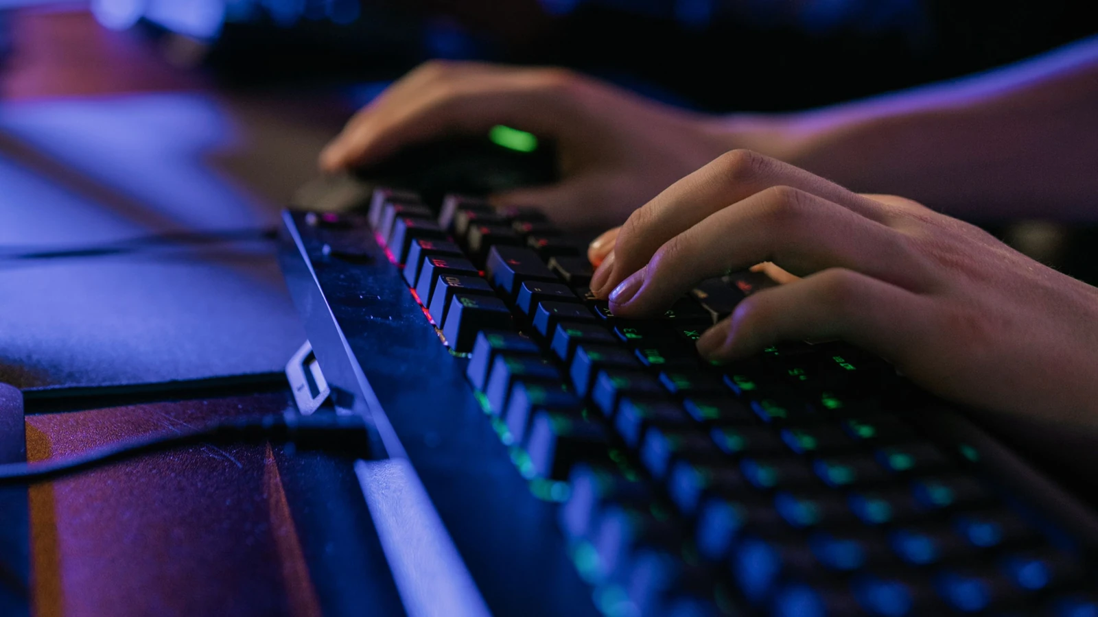 Hands use an illuminated keyboard and mouse at a PC gaming station, photographed by Alena Darmel for Pexels.