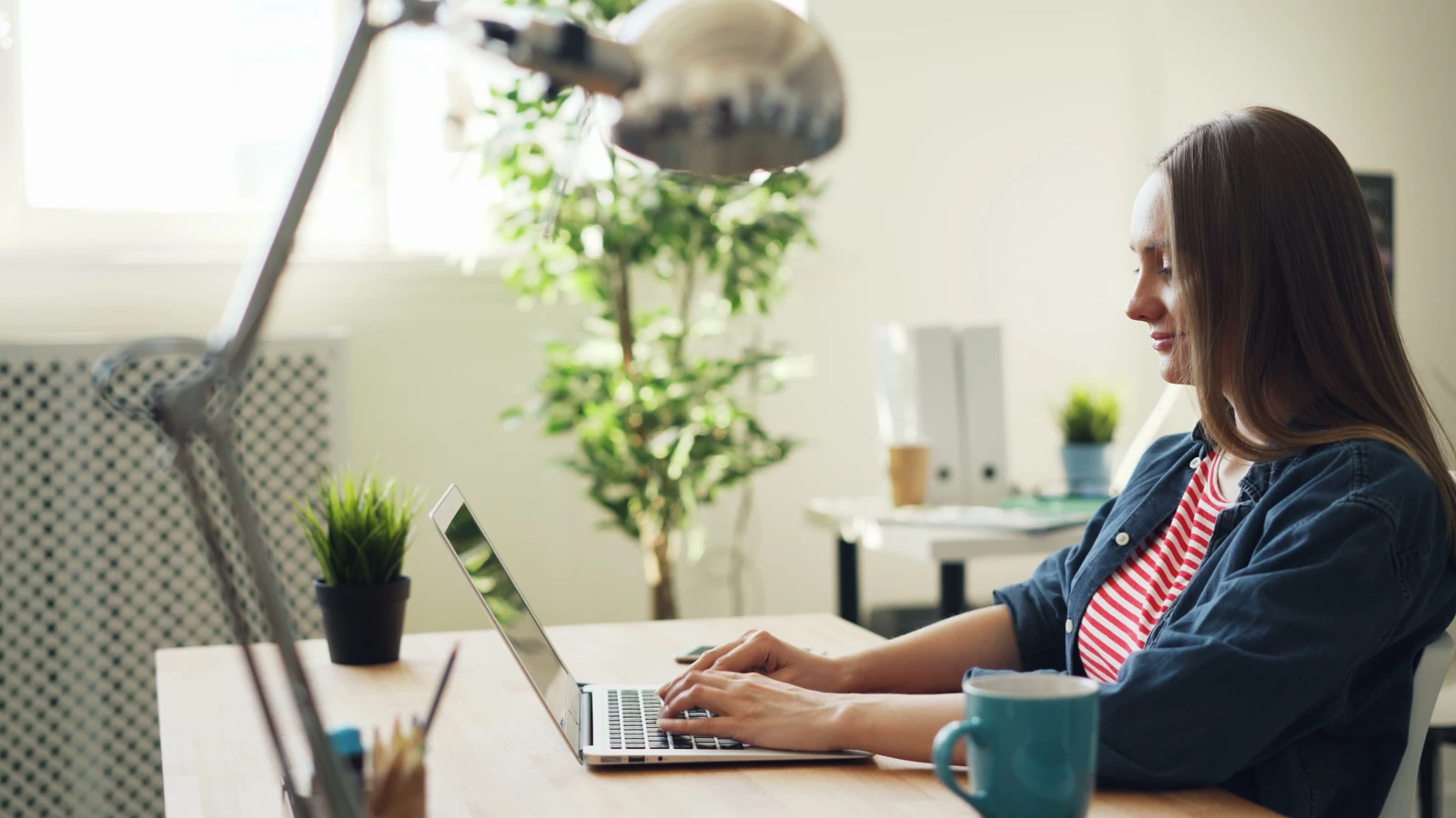 A woman works on a laptop at a desk beside office plants, a representative workplace photograph by Vitaly Gariev on Pexels.