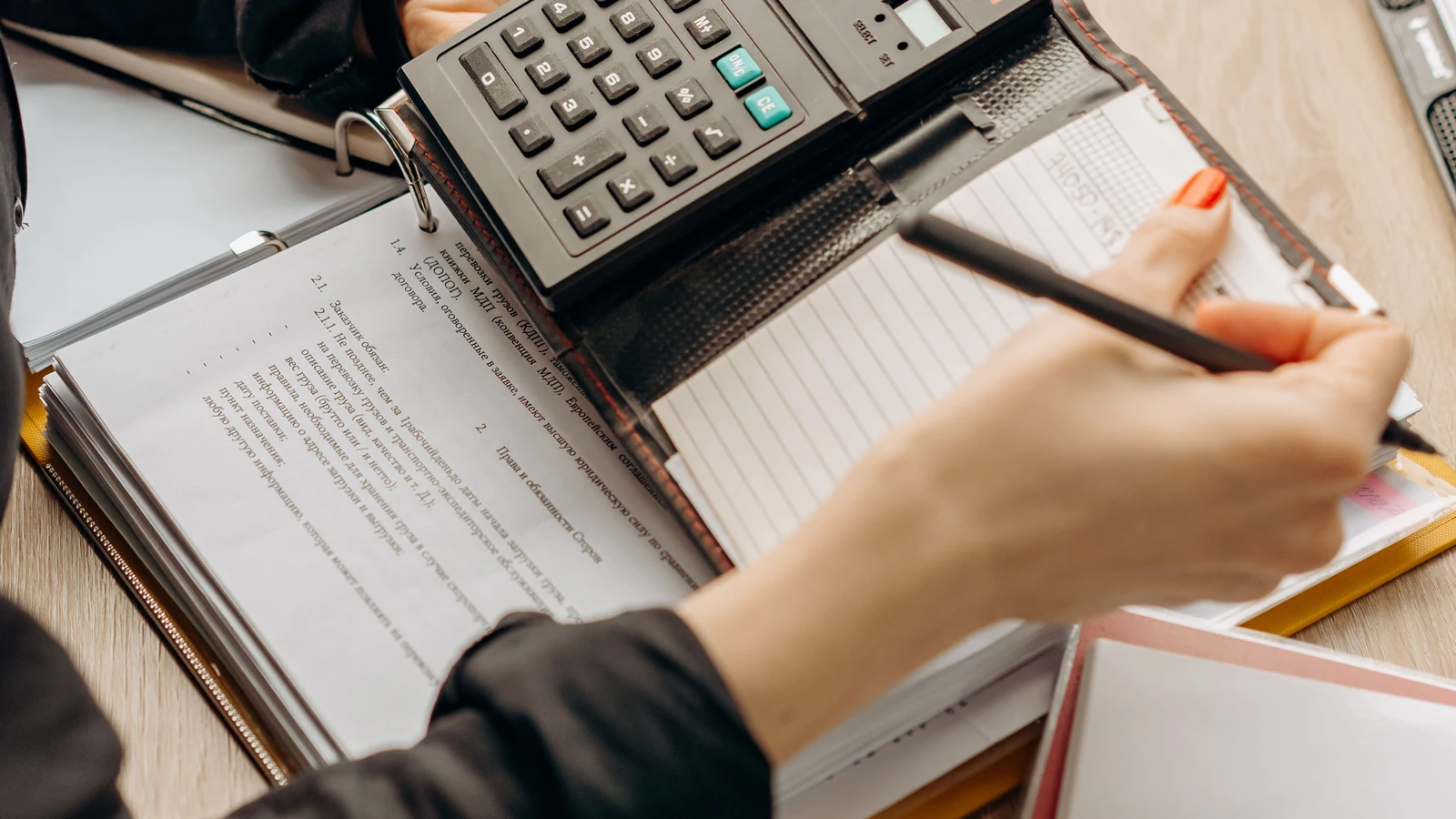 Hands use a calculator beside paperwork and office folders, a representative financial stock photograph by Mikhail Nilov via Pexels.