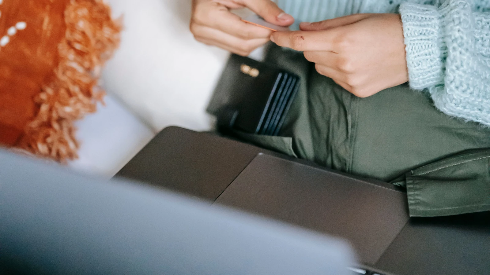 Hands hold a payment card above a laptop and open wallet, a representative stock photograph by Liza Summer via Pexels.