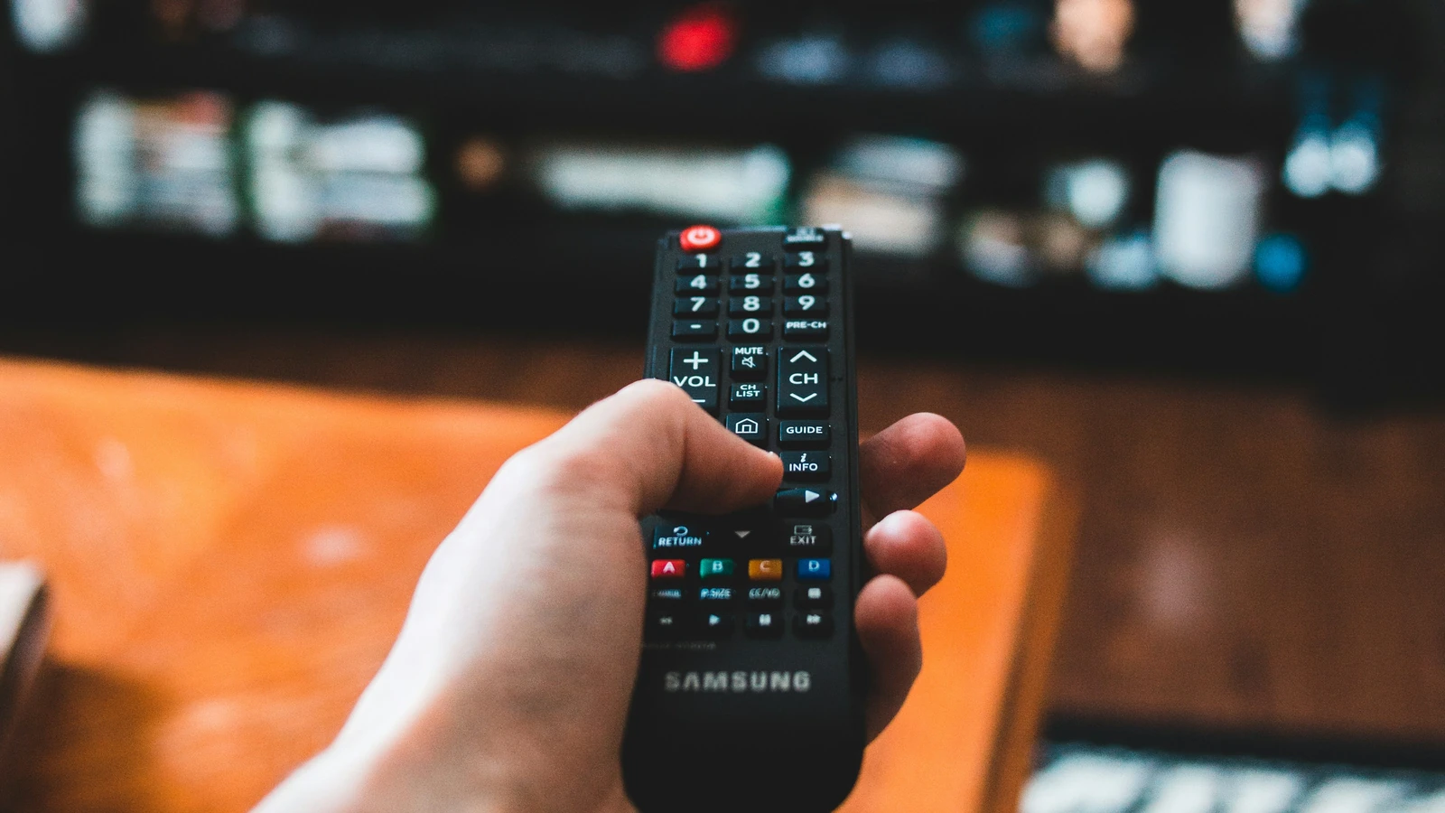 A hand holds a television remote in front of a blurred screen, photographed by Erik Mclean for Unsplash.