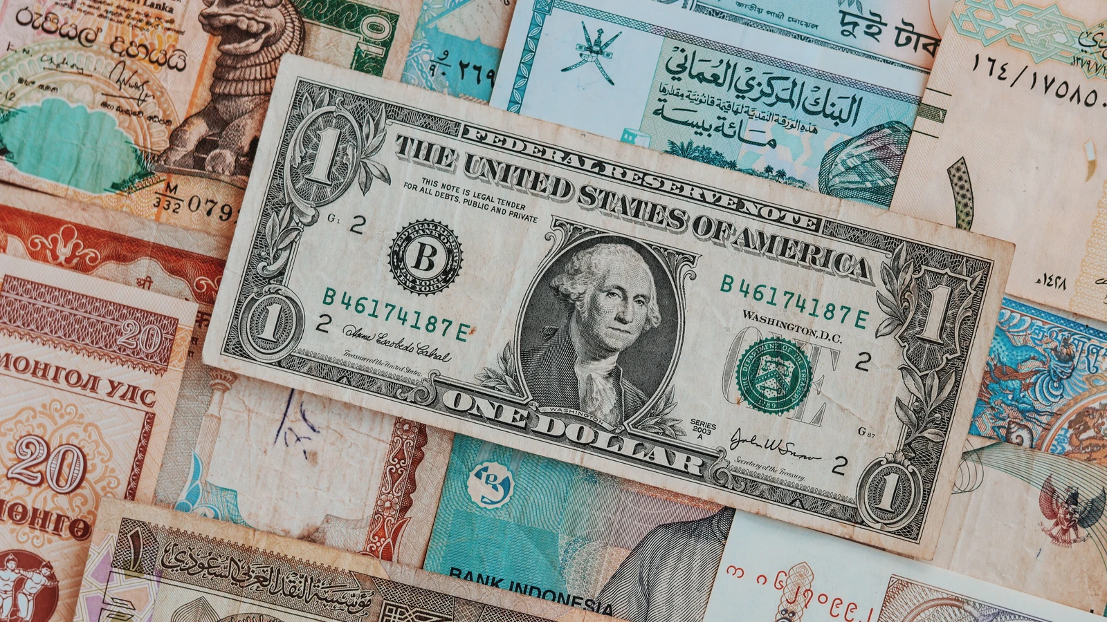 A US dollar bill lies across assorted international banknotes in a representative currency photograph by Pratikxox from Pexels.