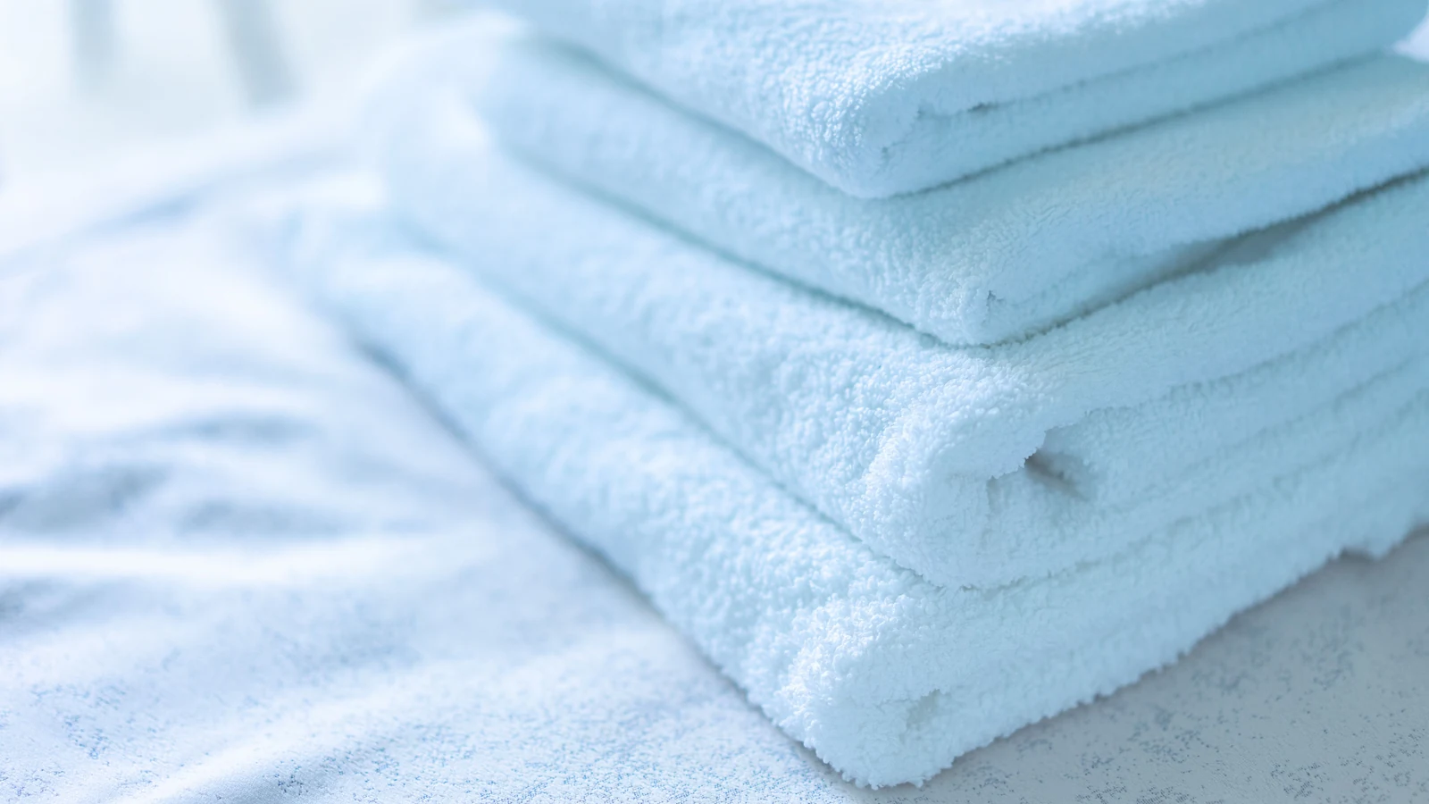 White cotton towels folded in a stack on a light surface. Photo by Atlantic Ambience via Pexels.