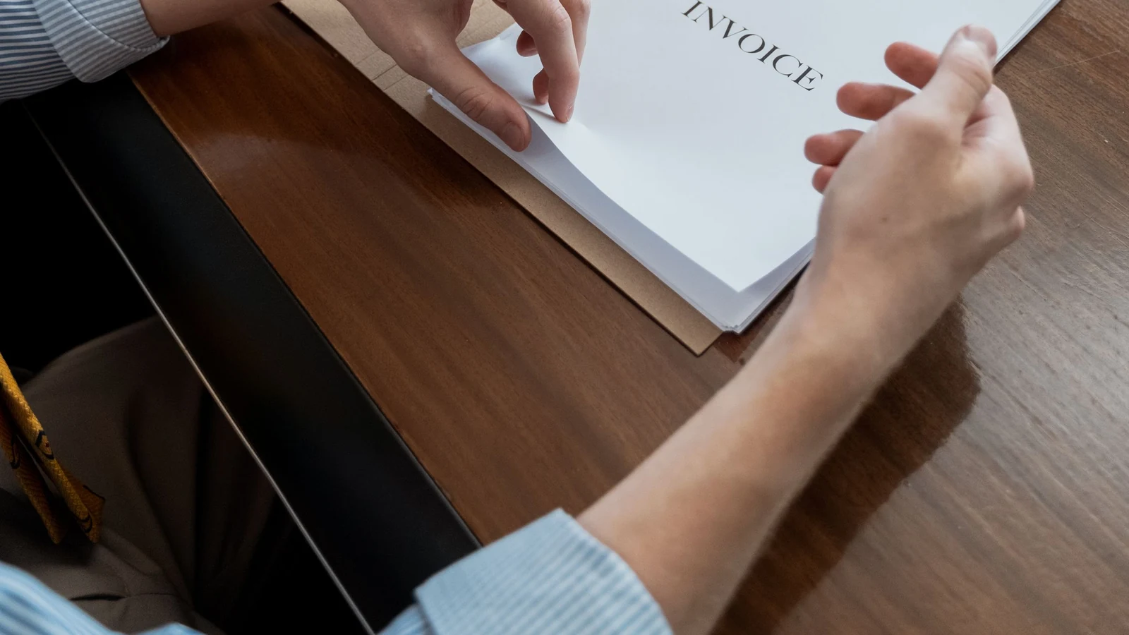 Hands review invoice paperwork on a wooden desk in a representative stock photograph by MART PRODUCTION/Pexels.