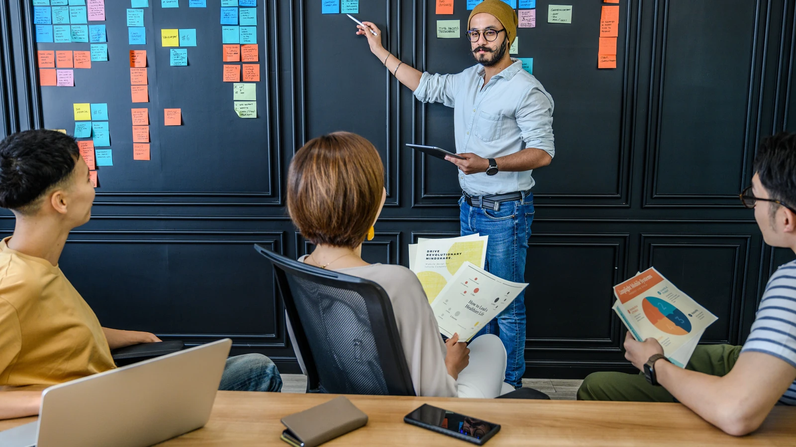 Colleagues discuss charts and colorful sticky notes in an office, a representative stock photograph by Ketut Subiyanto/Pexels.