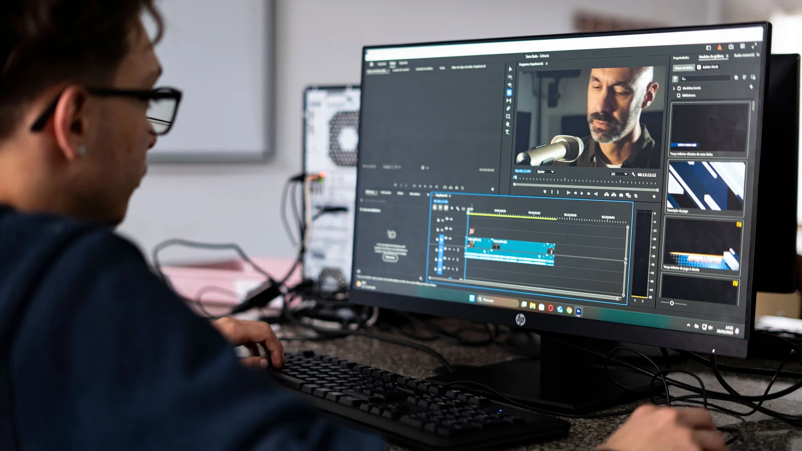 A video editor works at a desktop computer displaying editing software. Photo: André Eusébio / Pexels.