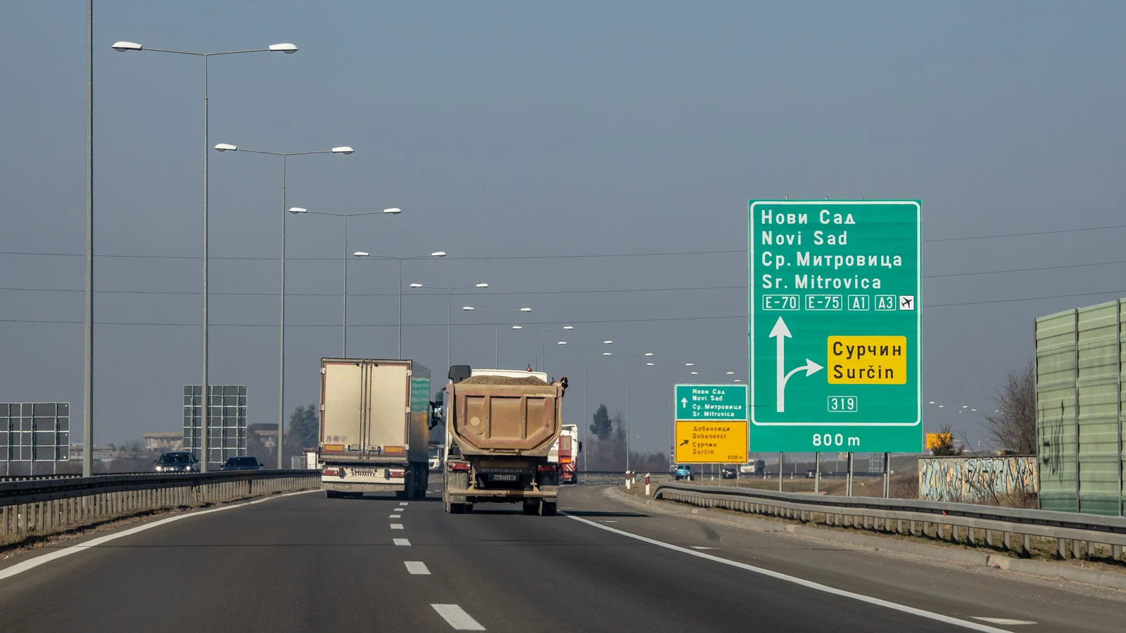 Trucks travel on a Serbian expressway beneath road signs. Representative photograph by Boris Hamer via Pexels.