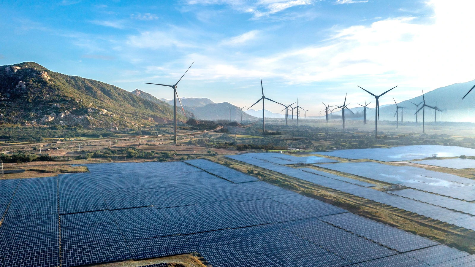 Wind turbines stand behind rows of solar panels in Vietnam, photographed by Quang Nguyen Vinh for Pexels.